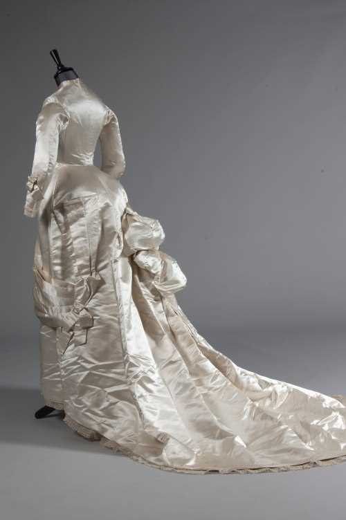 Lot 55 - An ivory satin bridal gown, late 1870s, of...