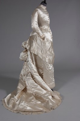 Lot 55 - An ivory satin bridal gown, late 1870s, of...