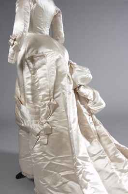 Lot 55 - An ivory satin bridal gown, late 1870s, of...