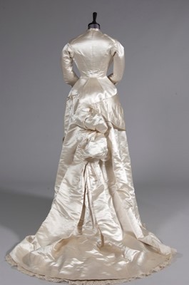 Lot 55 - An ivory satin bridal gown, late 1870s, of...