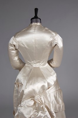 Lot 55 - An ivory satin bridal gown, late 1870s, of...
