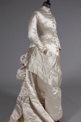 Lot 55 - An ivory satin bridal gown, late 1870s, of...